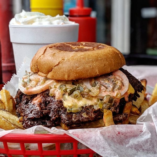 A Region burger with special sauce and pickles, fries, and a milkshake in a red basket.