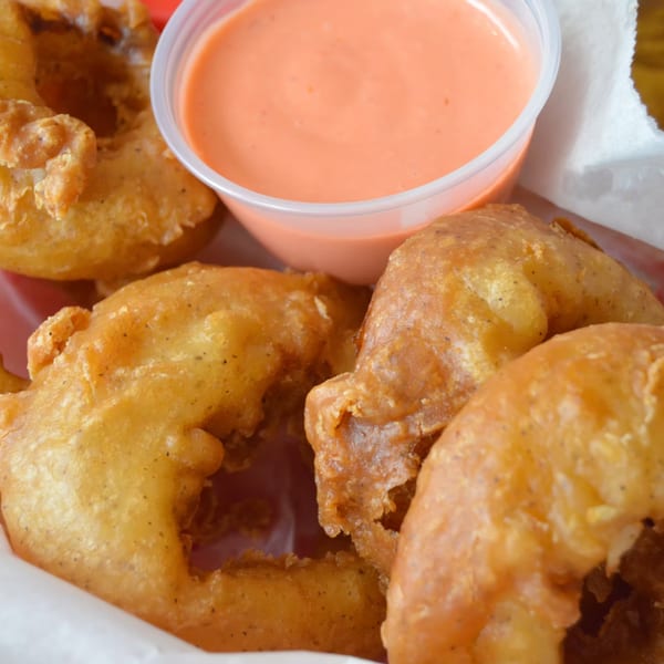 Golden-brown onion rings from The Region, served with a side of creamy orange dipping sauce.