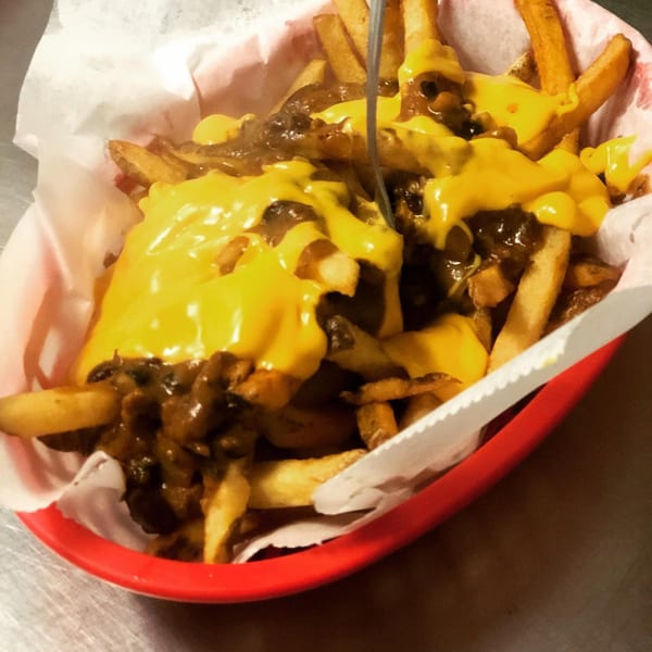 Chili cheese fries in a red basket with a fork, from The Region - Handcrafted Hamburgers.