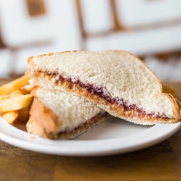 Peanut butter and jelly sandwich, cut in half, served with a side of french fries.