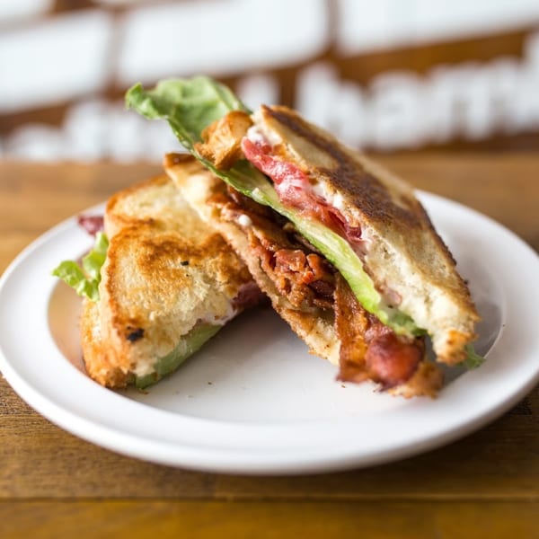 Two halves of a grilled cheese sandwich with bacon, lettuce, and tomato on a white plate.