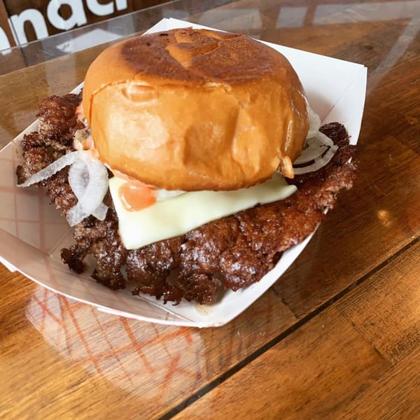A Region burger with a crispy patty, melted cheese, onions, and sauce in a paper tray.