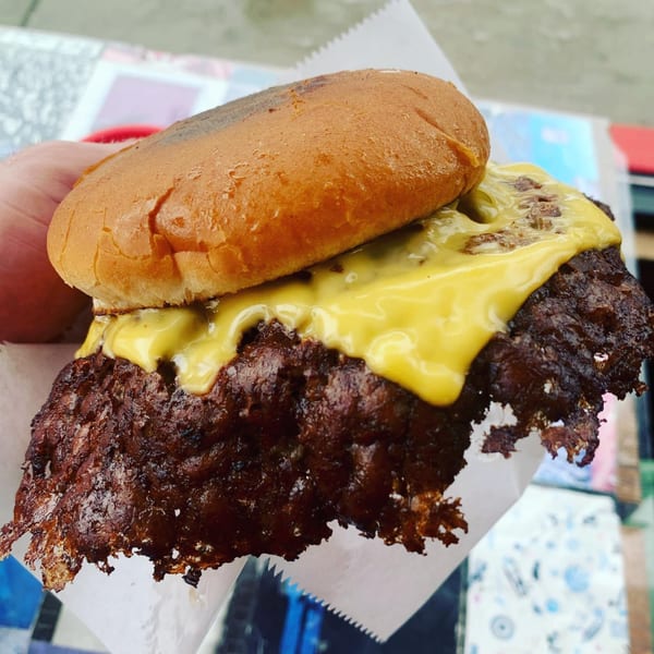 A hand holds a The Region burger with a crispy patty and melted cheese on a bun.